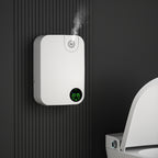 White electronic  Odor Removal Diffuser device with digital display attached to a black wall next to a toilet.