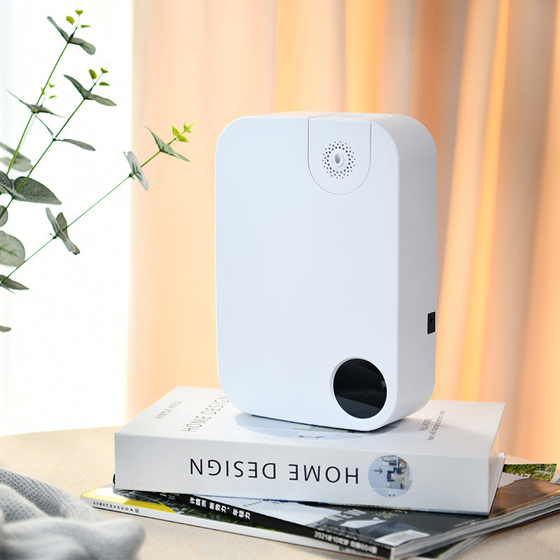 White electronic  Odor Removal Diffuser on a stack of books with a plant and warm-toned curtains in the background