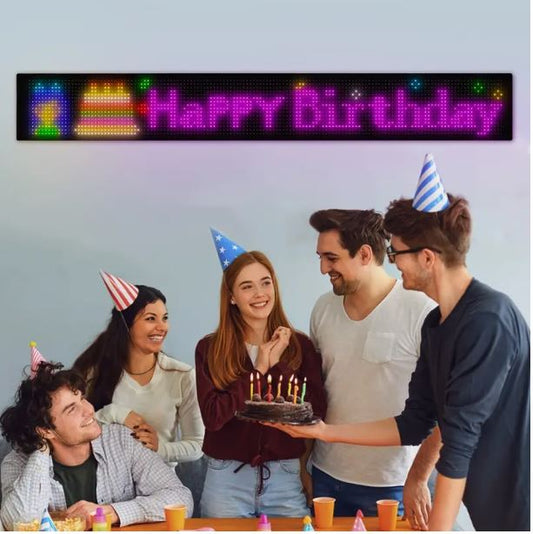 Group of friends celebrating a birthday with a LED sign displaying 'Happy Birthday'.