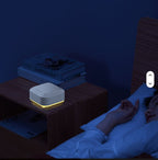 Small White Noise Sound device on a nightstand next to a person lying in bed