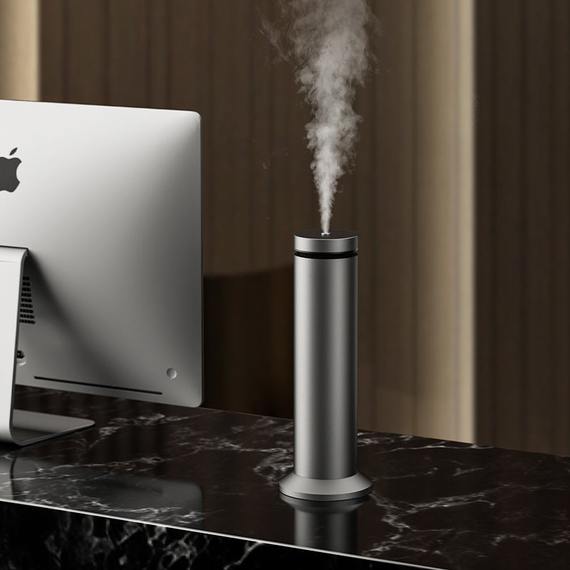 Silver humidifier emitting steam on a marble desk with a computer monitor in the background.