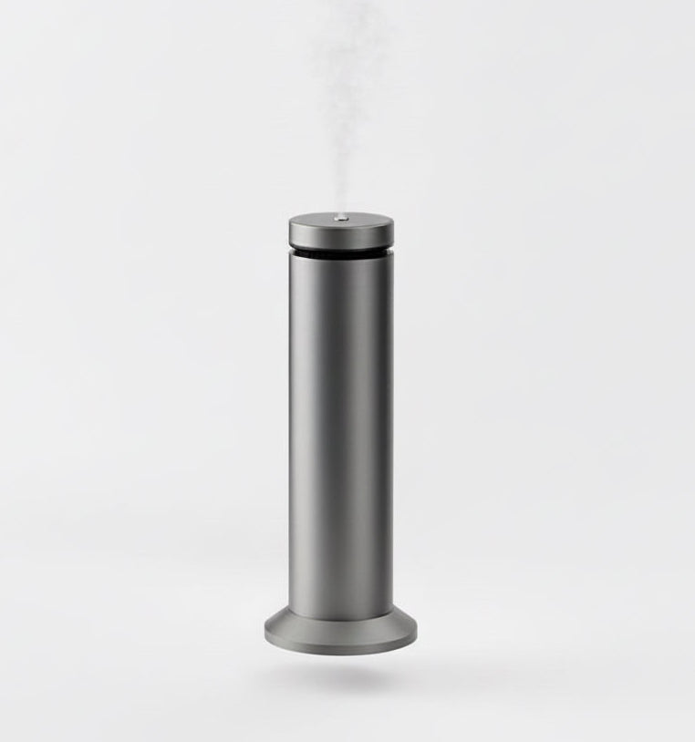 Silver humidifier emitting steam on a marble desk with a computer monitor in the background.