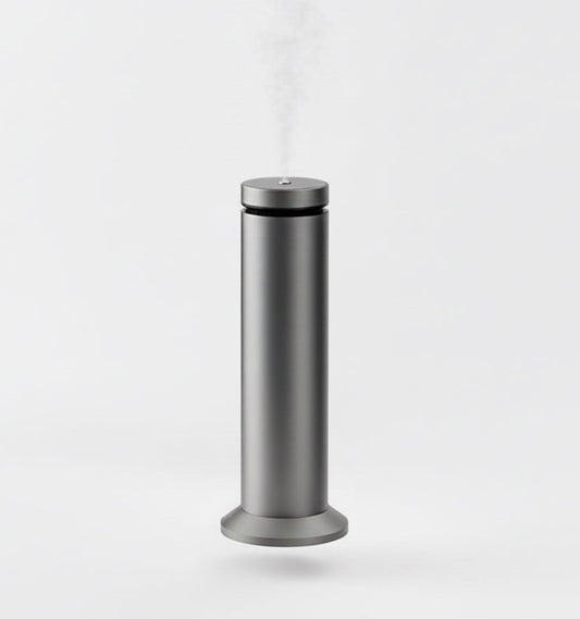 Silver humidifier emitting steam on a marble desk with a computer monitor in the background.